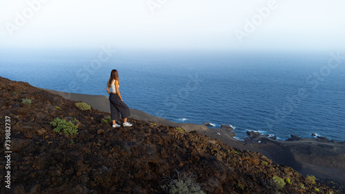 aerial drone view woman on the edge of a volcano crater looking at sea