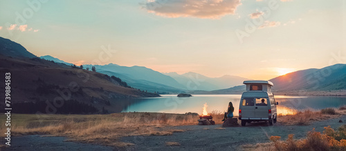 un van de camping garé à côté d'un lac, et une femme assise à côté d'un feu de camp photo