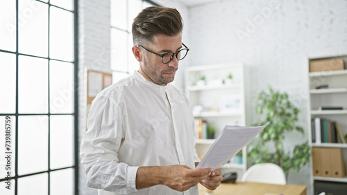 Attractive young hispanic male business manager, concentrated in reading an important document in the office, serious expression portraying success