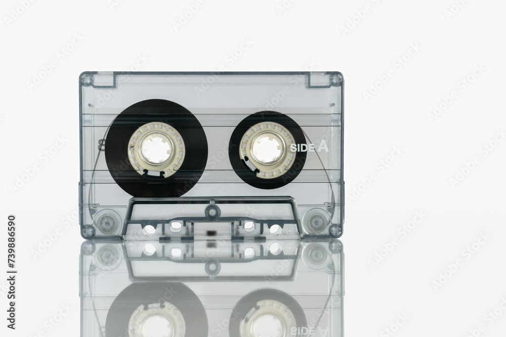 Fototapeta premium Audio cassette in a transparent case stands on a white background with reflection