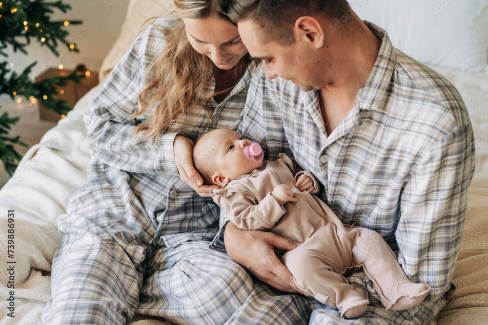 Mother and father are holding an adorable newborn baby sucking a pacifier. Family relationships.