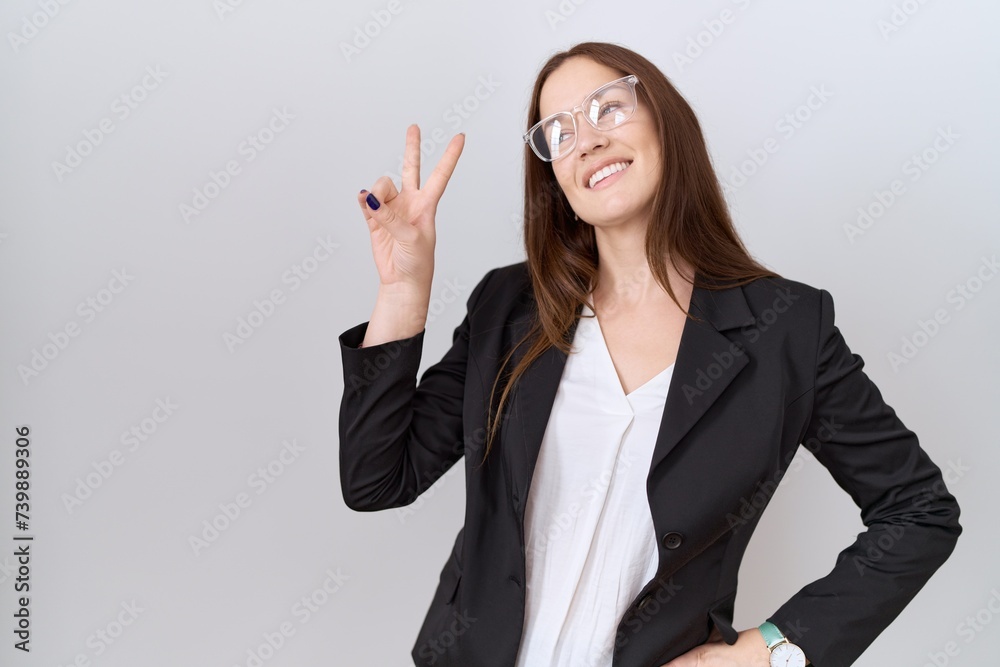 Beautiful brunette woman wearing business jacket and glasses smiling looking to the camera showing fingers doing victory sign. number two. Beautiful brunette woman wearing business jacket and glasses smiling looking to the camera showing fingers doing victory sign. number two.
