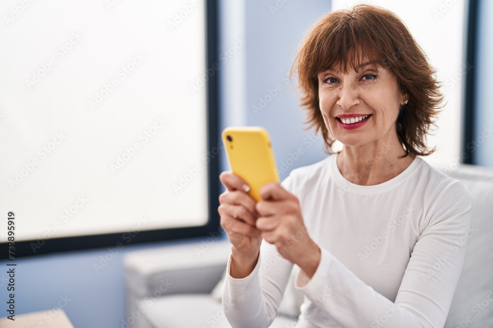 Middle age woman using smartphone sitting on sofa at home Middle age woman using smartphone sitting on sofa at home