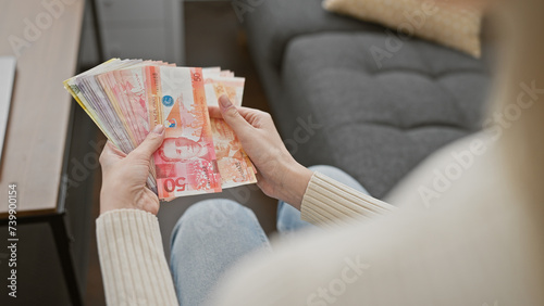 Young caucasian woman counting philippine pesos indoors, portraying an image of finance at home.