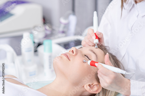 Pretty young woman getting microcurrent face therapy. Relaxed beautiful female patient receiving stimulating electric facial treatment from therapist at spa clinic