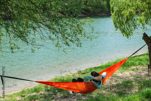 Woman in a cap lying in a hammock overlooking the river
