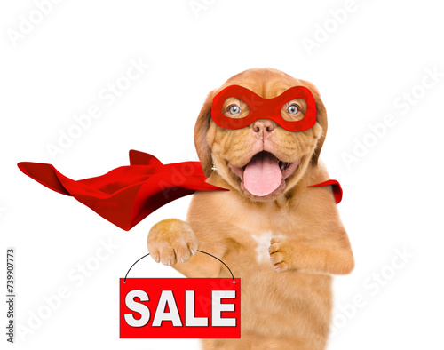 Funny Mastiff puppy with open mouth wearing superhero costume looking at camera and  showing signboard with labeled "sale". Isolated on white background