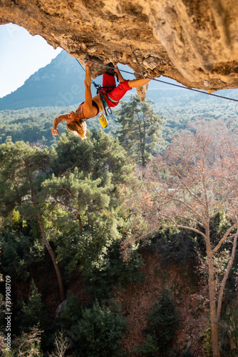 Girl climber on an overhanging rock. A sports woman climbs a rock against the backdrop of mountains. difficult movements in rock climbing.
