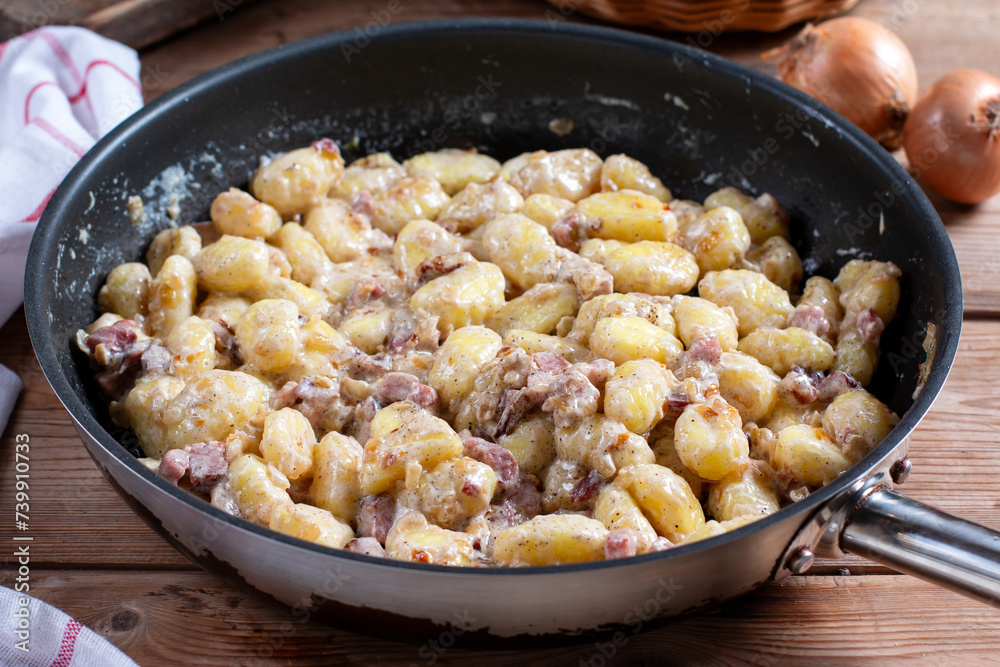 Close up view of potato gnocchi with bacon and sauce in pan on a wooden table.