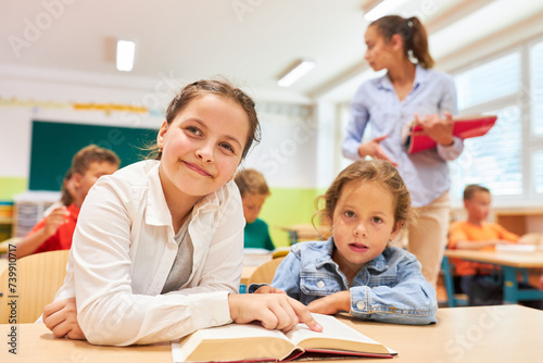 Girls sitting with book on bench in classroom