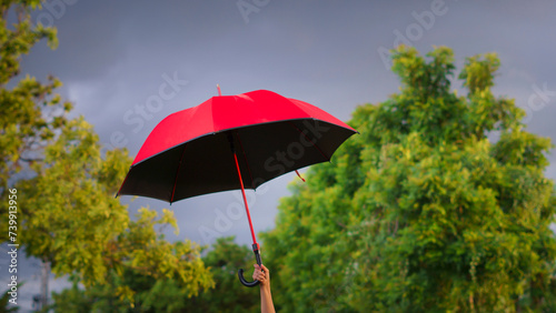 Woman holding a big red umbrella On a day when the sky is overcast and windy Looks like a storm is coming.