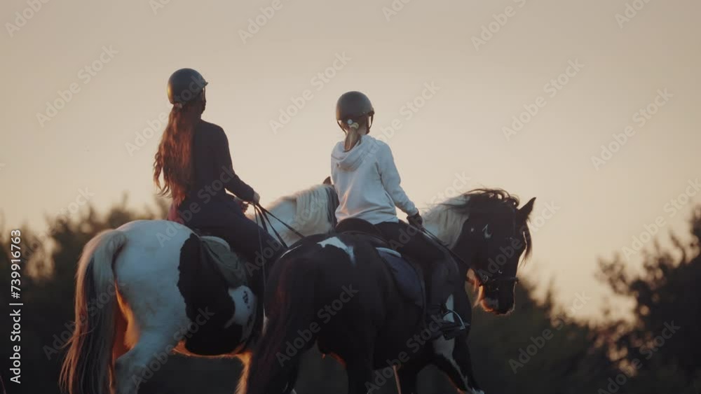 Two young girls horseback riding at golden sunset. Countryside activity with farm animals. Professional horse riders.