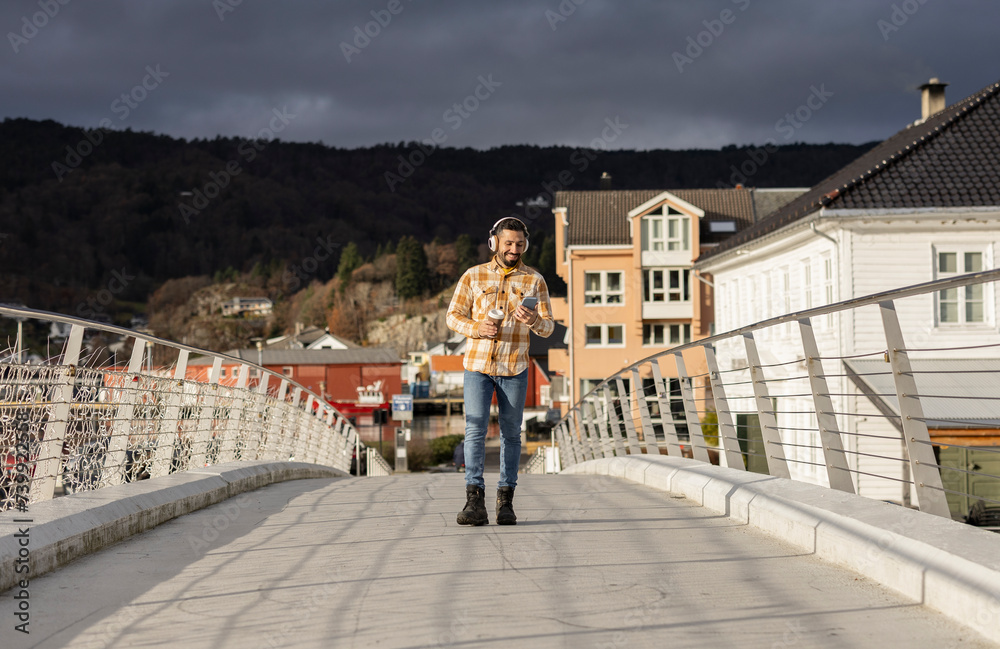 man listens to music with headphones and smart phone with a takeaway coffee tourist in Norway