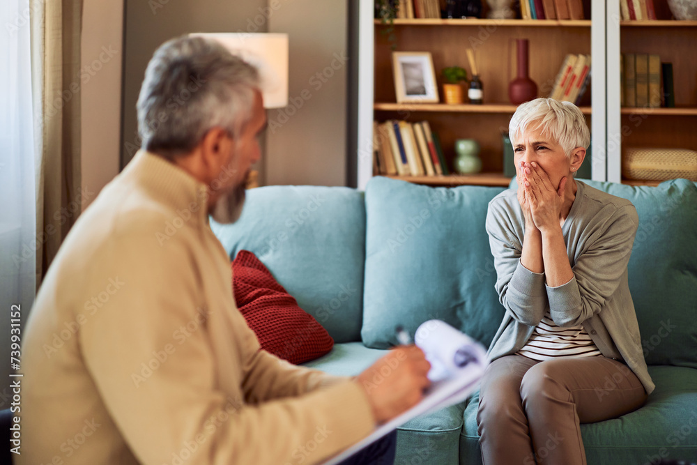 Fototapeta premium A shocked senior adult woman covering her mouth while listening to the bad news about her mental health from her male therapist