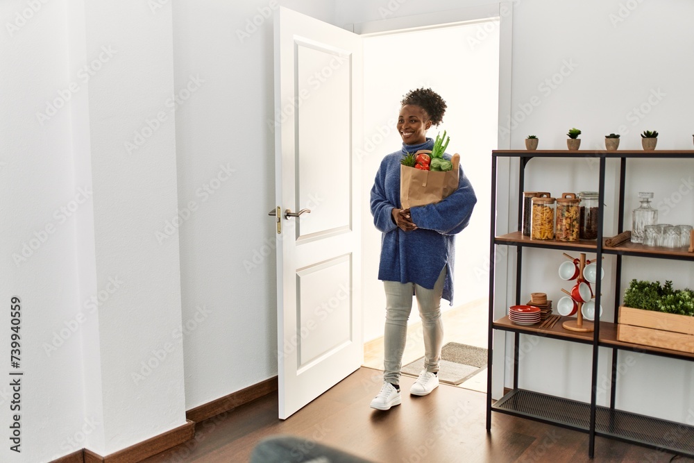 African american woman holding groceries bag walking through the door at home African american woman holding groceries bag walking through the door at home