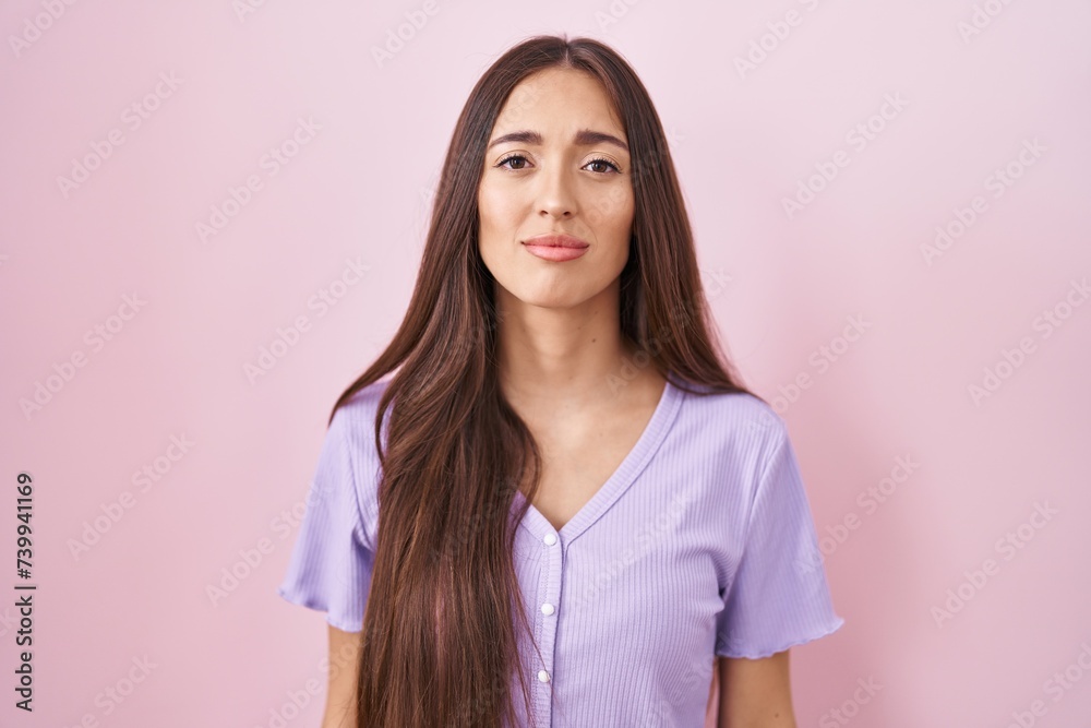 Fototapeta premium Young hispanic woman with long hair standing over pink background looking sleepy and tired, exhausted for fatigue and hangover, lazy eyes in the morning.