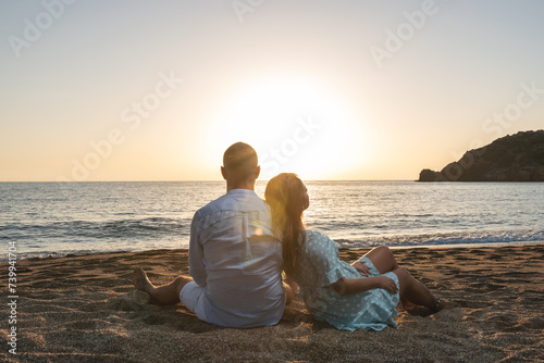 Happy couple in love  is seating on the beach during sunset or sunrise. Summer vacations.