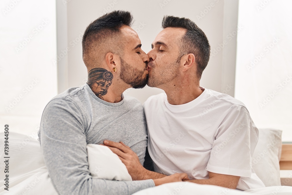 Two men couple sitting on bed hugging each other kissing at bedroom Two men couple sitting on bed hugging each other kissing at bedroom