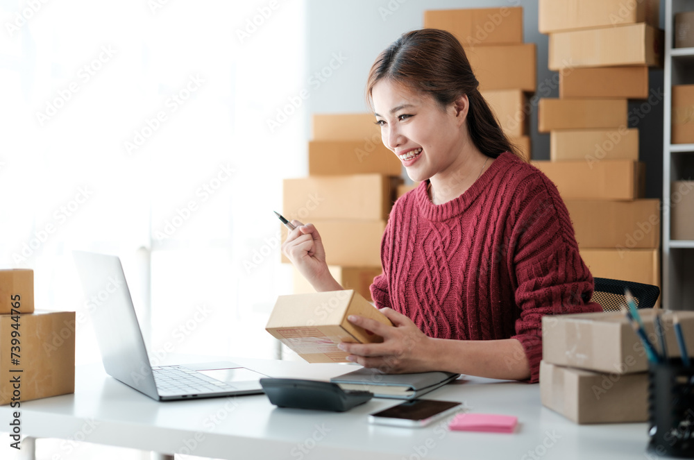 Startup SME small business entrepreneur of freelance Asian woman wearing apron using laptop and box to receive and review orders online to prepare to pack sell to customers, online sme business ideas. Startup SME small business entrepreneur of freelance Asian woman wearing apron using laptop and box to receive and review orders online to prepare to pack sell to customers, online sme business ideas.