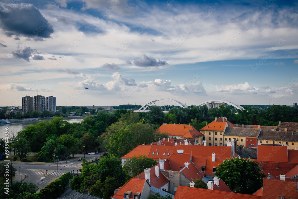 Obraz premium Petrovaradin, Serbia - May 09, 2023. Petrovaradin is historic town on right bank of Danube in Serbia, part of Novi Sad. Top view of the tiled orange roofs with white chimneys and magic cloudy sky