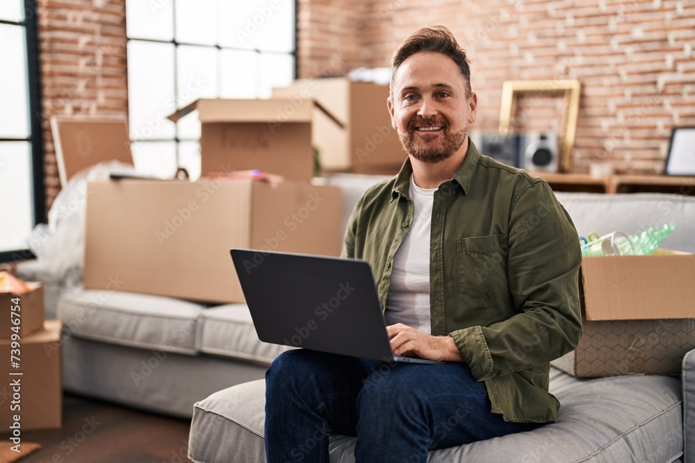 Young caucasian man using laptop sitting on sofa at new home Young caucasian man using laptop sitting on sofa at new home