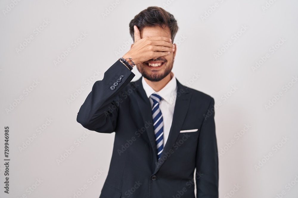 Young hispanic man with tattoos wearing business suit and tie smiling and laughing with hand on face covering eyes for surprise. blind concept. Young hispanic man with tattoos wearing business suit and tie smiling and laughing with hand on face covering eyes for surprise. blind concept.
