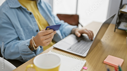 Hispanic man holding credit card while using laptop at office workspace