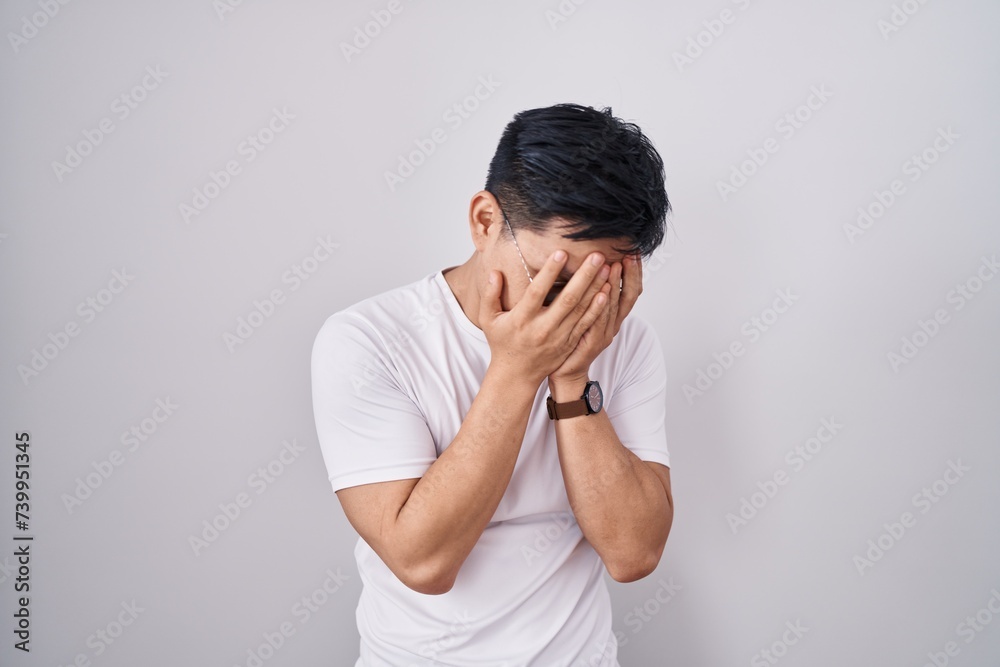 Young asian man standing over white background with sad expression covering face with hands while crying. depression concept. Young asian man standing over white background with sad expression covering face with hands while crying. depression concept.