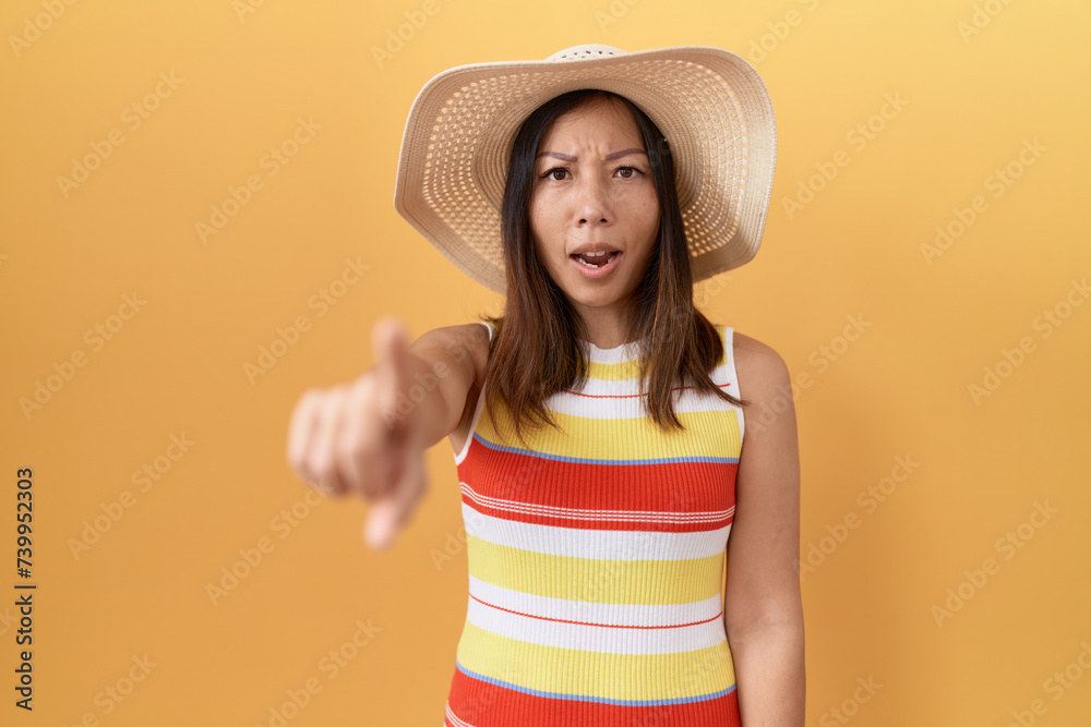 Middle age chinese woman wearing summer hat over yellow background pointing displeased and frustrated to the camera, angry and furious with you Middle age chinese woman wearing summer hat over yellow background pointing displeased and frustrated to the camera, angry and furious with you