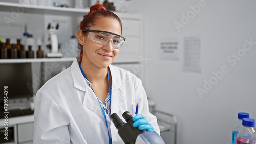 Radiant young redhead woman scientist smiling while performing biolological analysis with microscope in the heart of a high-tech lab photo