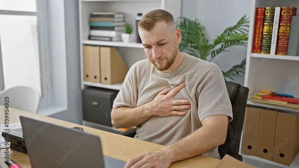 Young caucasian man experiencing chest pain while working at his office desk, indicating potential health issue.