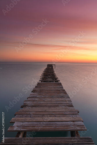 Fototapeta Naklejka Na Ścianę i Meble -  vertical sunrise seascape with an old wooden dock leading out into the calm ocean waters