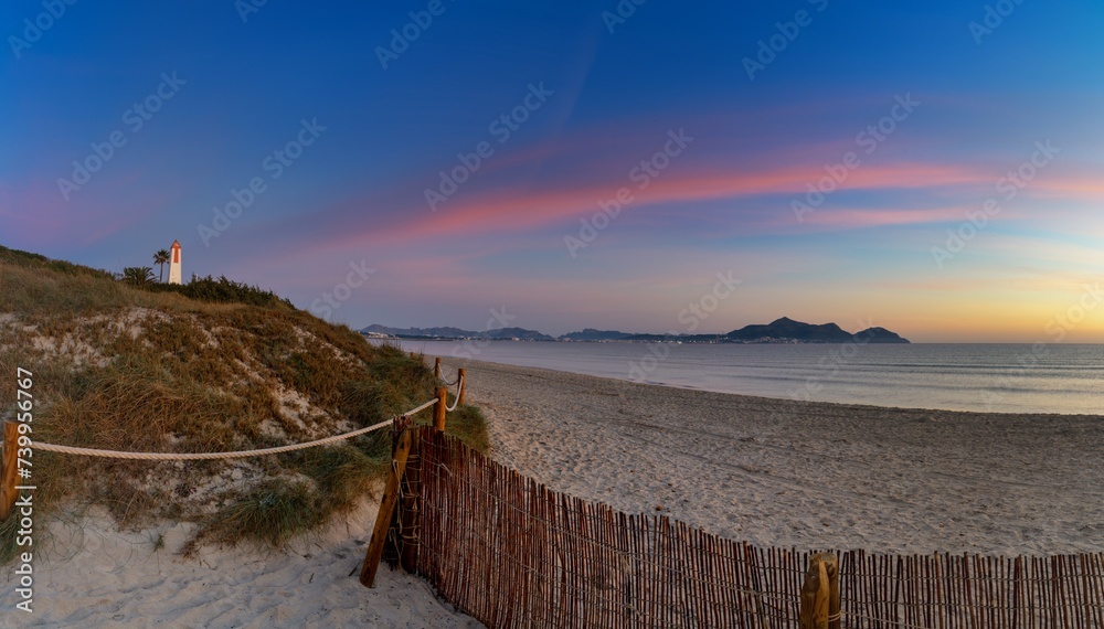 Playa del Muro beach with sand dunes and a view of the historic maritime observation towers and the town of Alcudia in the background