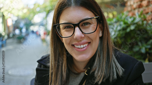 Happy, adult, brunette woman wearing glasses, sitting at a cafe terrace on a sunny day with street background © Krakenimages.com