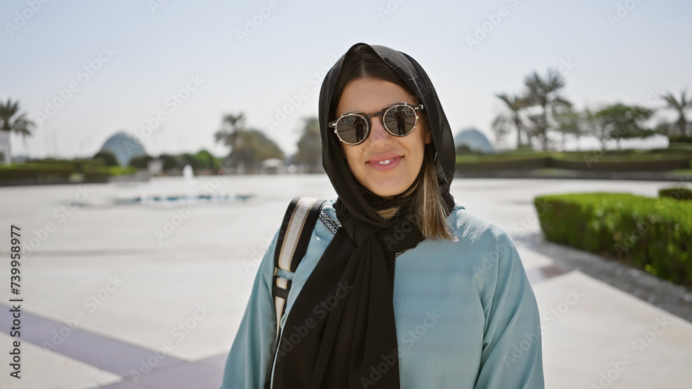 Portrait of a smiling young woman in sunglasses and a hijab at an islamic mosque in abu dhabi, uae.