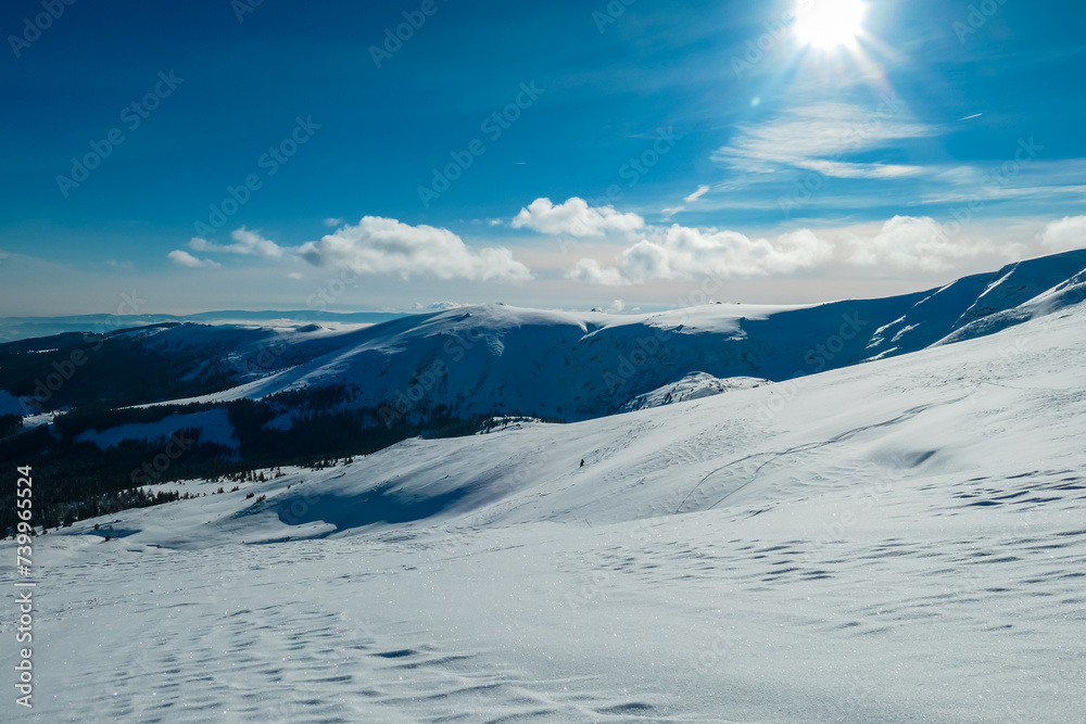 Snow covered meadow with panoramic view of hills and mountains seen from Kor Alps, Lavanttal Alps, Carinthia Styria, Austria. Winter wonderland in Austrian Alps. Ski touring on untouched landscape