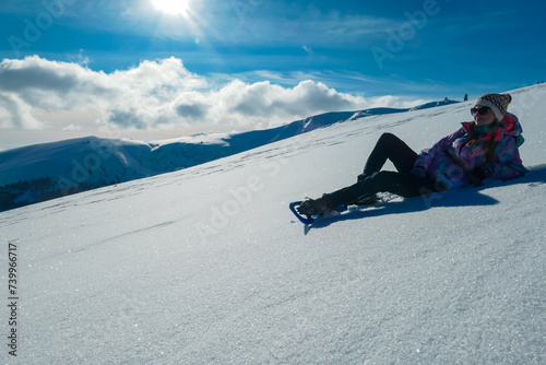 Woman in snowshoes lying in snow with view of mountains of Kor Alps, Lavanttal Alps, Carinthia Styria, Austria. Winter wonderland in Austrian Alps. Looking at majestic summit peak Grosser Speikogel photo