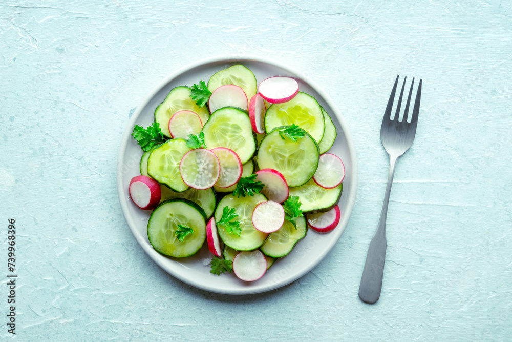 Fresh cucumber and radish salad with parsley, overhead flat lay shot with a fork. Simple vegan recipe on a slate background. Healthy diet Fresh cucumber and radish salad with parsley, overhead flat lay shot with a fork. Simple vegan recipe on a slate background. Healthy diet