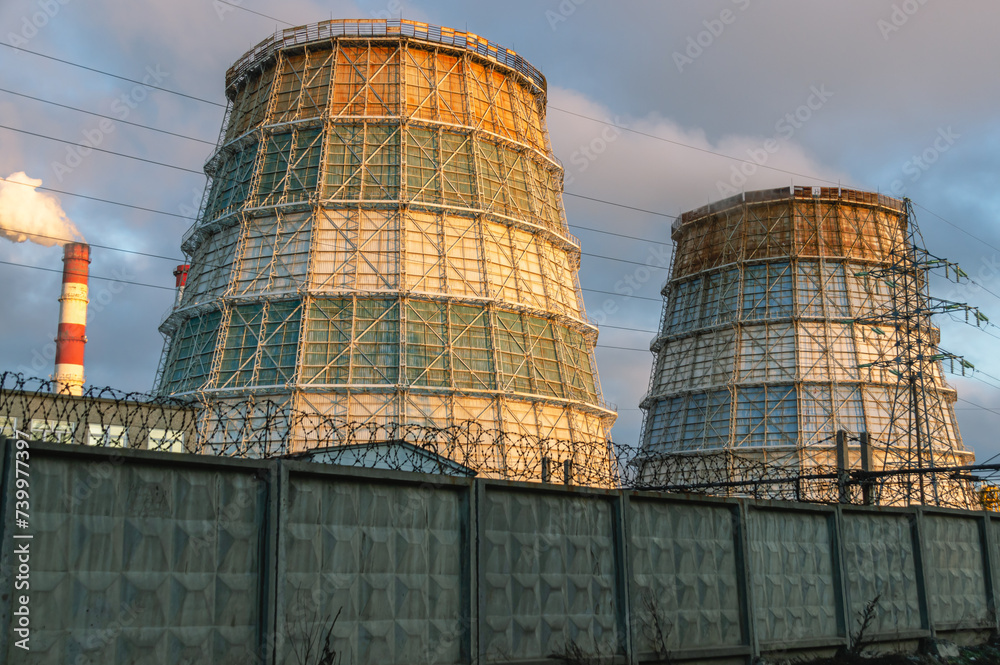 Large cooling towers of thermal power plants. White steam comes out of the cooling tower against the blue sky. Cooling tower for cooling water. A source of thermal energy in district heating systems.
