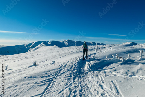 Woman in snowshoes on way to majestic summit peak Grosser Speikogel in Kor Alps, Lavanttal Alps, Carinthia Styria, Austria. Winter wonderland in Austrian Alps. Idyllic ski touring trail. Frozen fence photo