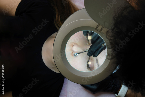 Cosmetologist Performing Facial Cleansing Procedure. A cosmetologist during a facial cleansing session using special equipment to treat the client's skin, view through a magnifying lamp. 