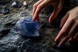 fingers touching a raw sapphire crystal against a dark stone surface