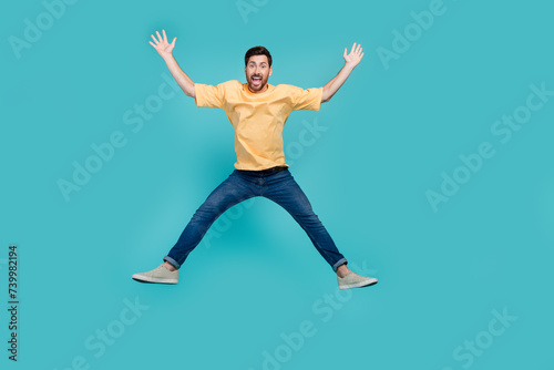 Full body length photo of active man in yellow t shirt and jeans raised hands up seems like star figure isolated on blue color background photo