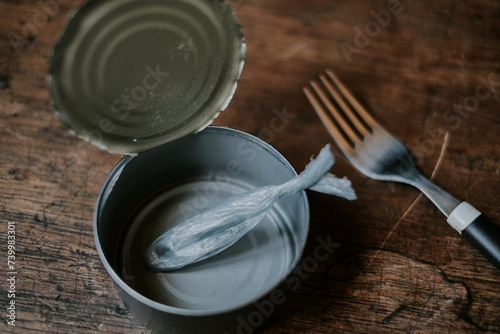 A conceptual representation of food waste and sustainability, featuring an open tin can with a plastic bag twisted to resemble a piece of food, next to an unused fork on a wooden surface photo