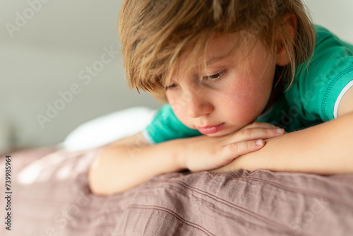 A thoughtful boy lies on the sofa . The child is sad alone at home. Childhood boredom and sadness concept. . High quality photo