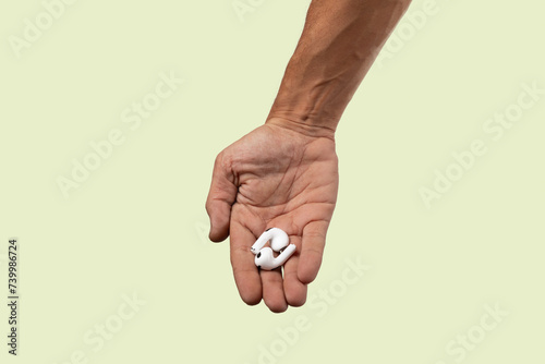 Male hand holding white earbuds on light green background.