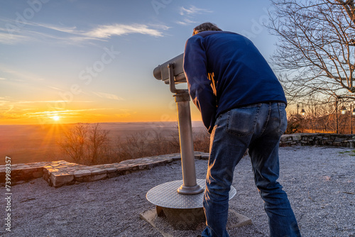 Mature Caucasian man using a mounted telescope to watch a scene at sunset, Cheaha State Park, Alabama photo