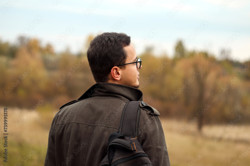 Back view tourist adventurous man with backpack stands on fall nature background. Man enjoys inspiring epic landscape. Blurred Back view tourist adventurous man with backpack stands on fall nature background. Man enjoys inspiring epic landscape. Blurred