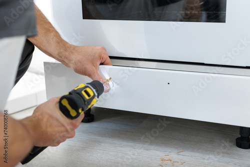 Worker installs a new handle on a white cabinet with a screwdriver.