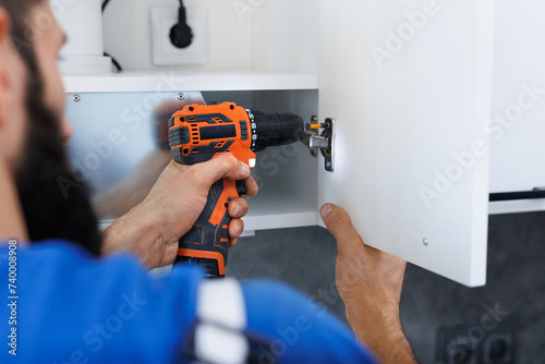 A man in uniform screws the kitchen cabinet doors with an electric screwdriver.